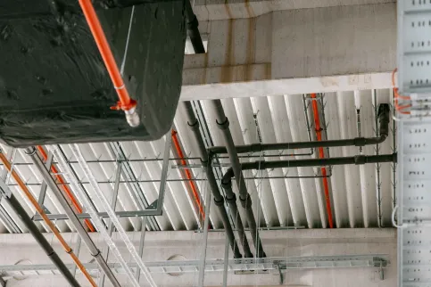 Die Entwässerung läuft unter dem Hallendach über Sammelleitungen als Druckentwässerung in schmalen Rohren (DN 70). (Die roten Leitungen sind Sprinkler für den Brandschutz.)