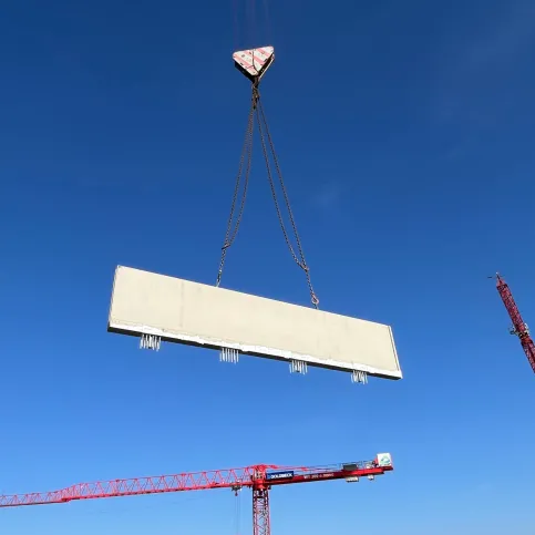 Effizient Bauen bedeutet bauzeitenflexibel: Schöck TELLIGENT® bietet Produktlösungen, die einen hohen Vorfertigungsgrad der Bauteile ermöglichen und damit just-in-time auf die Baustelle geliefert werden können. Im Bild: Ein Brüstungselement für die Attika mit Schöck Isokorb® CXT Typ A wird per Kran eingehoben.