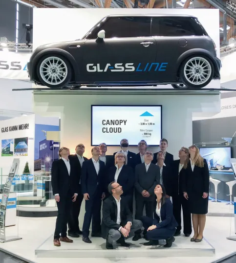 Hohen Belastbarkeit: Das GLASSLINE Messeexponat, ein 3,00 x 1,90 m großes Glasvordach CANOPY cloud, trägt einen Mini mit 900 kg.