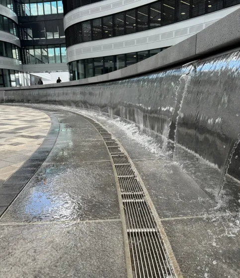 Die Wasserfall-Wand – das zentrale Gestaltungselement im Innenhof – wird durch die ACO Inotec 625 Überlauf- und Rücklaufrinnen aus Edelstahl entwässert.