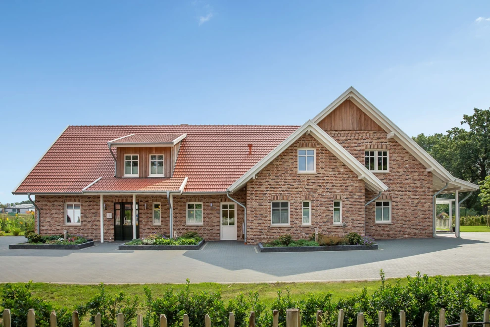 Der Doppelmuldenfalzziegel Tradition in rotbraun, zusammen mit der Klinkerfassade aus verschiedenen, rötlichen Farbtönen, ergeben ein Einfamilienhaus im Landhausstil.